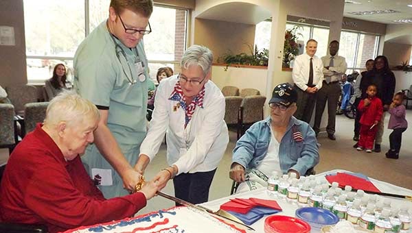 Vincent “Buddy” Lankford, left, gets help from Will Mason and Laurie Ross in cutting the cake with a sword during a reception to honor veterans on Monday in Southampton Memorial Hospital. Lankford and Edward Young, far right, are veterans of World War II. -- STEPHEN H. COWLES | TIDEWATER NEWS