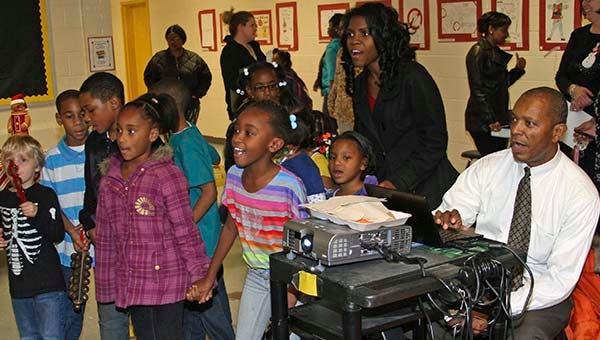 Clinton Smith, art teacher, is projecting the words to a song on the screen karaoke style, while the S.P. Morton students and music teacher Twynnette Anderson sing along to the holiday-themed tunes. -- FRANK DAVIS | TIDEWATER NEWS