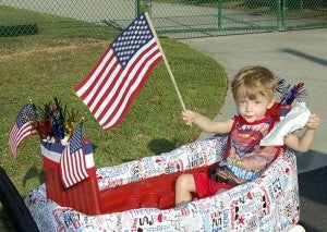 Christopher Fike, 2, of Windsor, holds up his flag as he is carted down the parade. -- Merle Monahan | Tidewater News