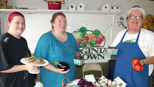 Cameron Stewart, left, Kathryn Dallabrida and Donna DeGroat hold up samples of what’s sold at the Main Street Farmer’s Market in Ivor. In front of them is a display of locally made crafts. -- STEPHEN H. COWLES | TIDEWATER NEWS