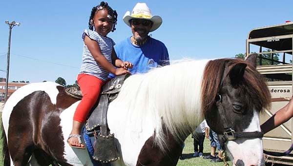 Naijah Boone, 4, of Franklin, smiles big as Ken Wright, Buffalo Riders of Hampton Roads president, prepares her to ride the pony. -- FRANK DAVIS | TIDEWATER NEWS