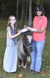 Madelyn Cosby, left, presents a check to Cyndi Raiford, the director of Graz’n Acres, for $2,600. Pictured with them is Lucky, one of the center’s miniature horses. -- SUBMITTED