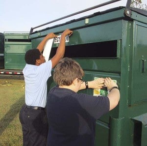 Reuben Leonard and Connor McCoy put stickers on the bins to show they're intended for depositing recyclable items. At left is David Felton from TFC, who is delivering the containers. -- SUBMITTED