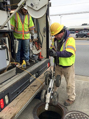 Michael Krewinghaus, left, and Dennis Mitchell of Prism Contractors and Engineers Inc., lower a camera attached to a tractor into a storm drain on Armory Drive. Stephen Cowles | The Tidewater News