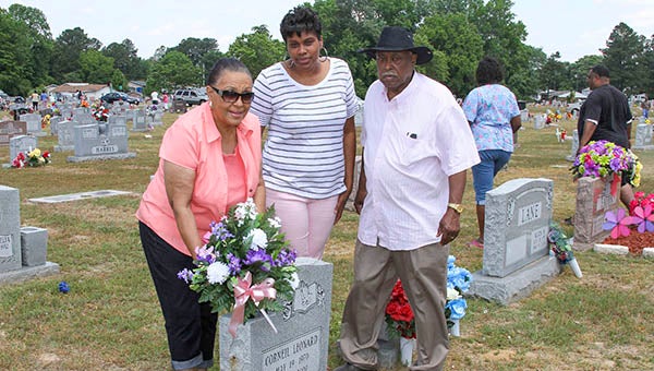 Diane Leonard, left, places flowers on the grave of her son, Corneil Leonard, as family member Kia Vinson, and her husband Ivan Leonard look on.  -- FRANK DAVIS | THE TIDEWATER NEWS