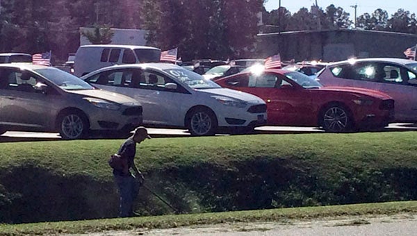 Across the street from The Tidewater News. a young man cuts grass at the ditch in front of the car dealership.